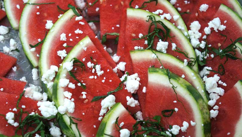 close up of watermelon wedges with basil and feta on a tray