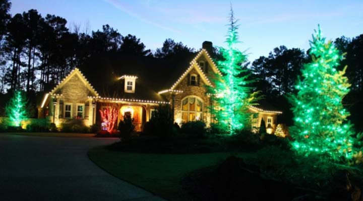 home decorated with with white lights and green-lit trees on yard