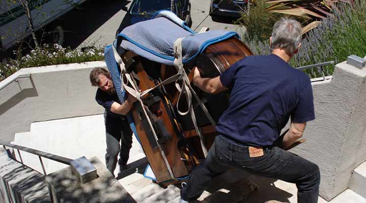 crews move a baby grand piano up stairs